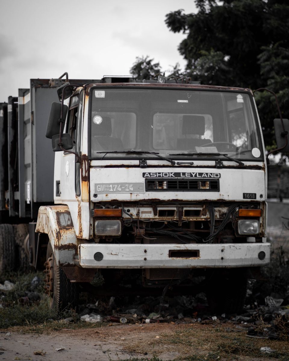 Aged, rusty truck abandoned outdoors amid nature with a broken grille.